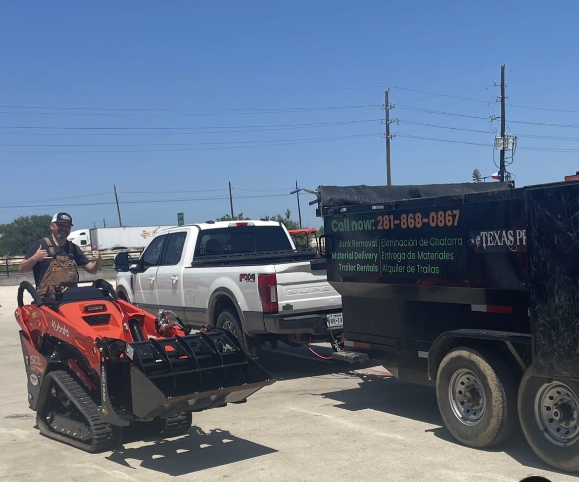Kubota SCL1000 with a grapple beside a Long Boy truck and dump trailer