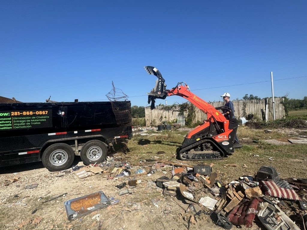 Kubota SCL1000 with a grapple loading demolition debris next to a Long Boy dump trailer